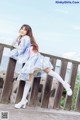 A woman in a blue and white dress posing on a wooden fence.