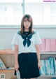 A woman in a school uniform standing in front of a bookshelf.