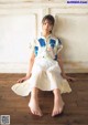 A woman sitting on a wooden floor wearing a white skirt.