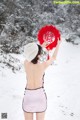 A woman in a pink dress holding a red fan in the snow.