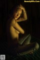 A naked woman sitting on a bed in the dark.