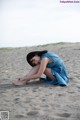 A woman in a blue dress sitting on the sand.