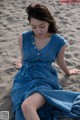 A woman in a blue dress sitting on the sand.