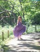 A woman in a purple dress walking down a path in the woods.