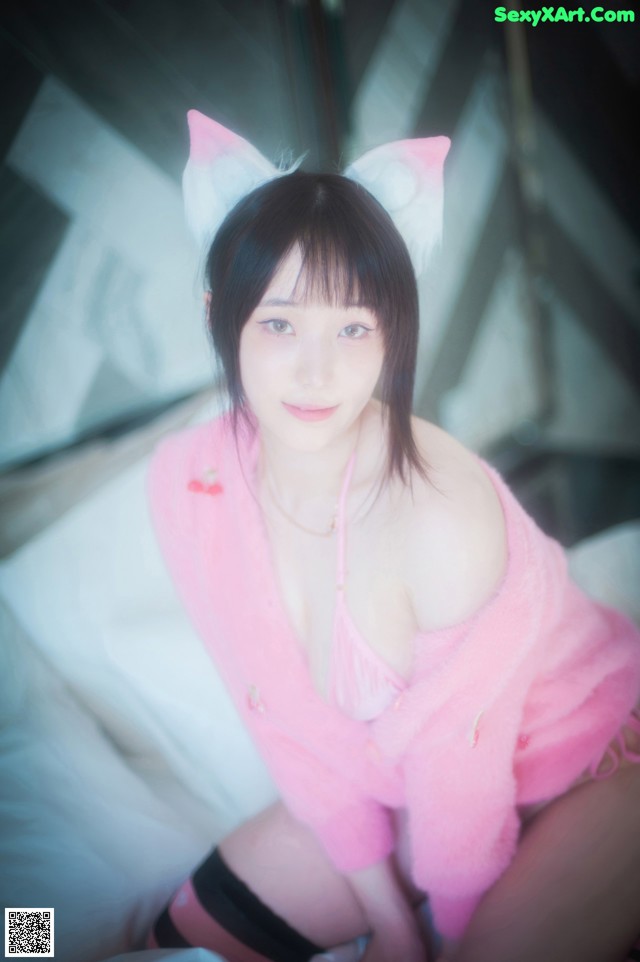 A woman in a pink outfit sitting on a bed.