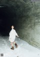 A woman in a white sweater is walking through a tunnel.