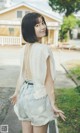 A woman in a white top and denim shorts standing on a sidewalk.