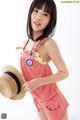 A young woman in a red and white striped romper holding a straw hat.