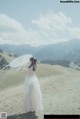 A woman in a white dress holding an umbrella in a field.