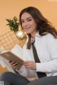 A woman in a white shirt and tie sitting on a bed reading a book.